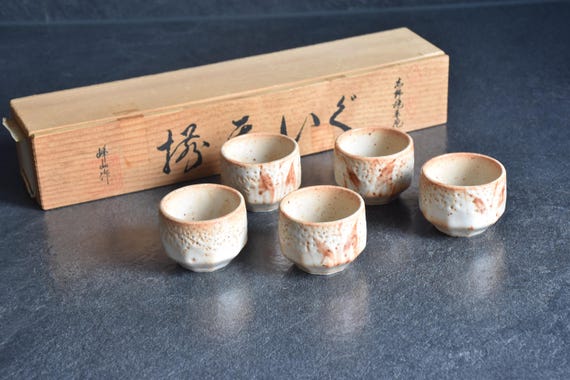 Set of 5 Shino ware ceramic guinomi sake cups displayed with wooden storage box angled