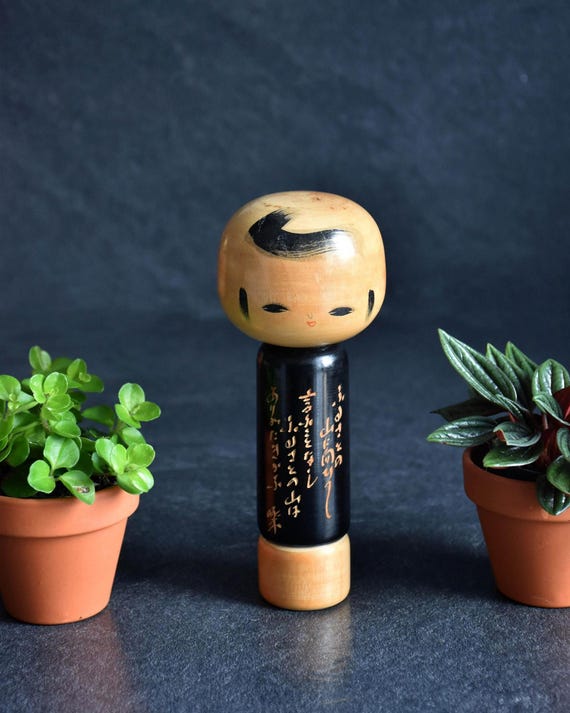 Japanese Kokeshi doll with poem, featuring a black wooden body with calligraphy and natural wood head.