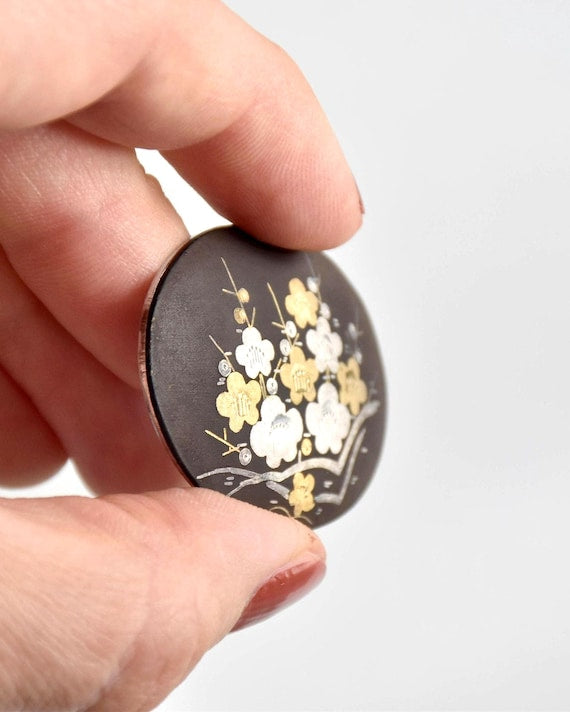 Zogan Plum Blossom Brooch held at an angle to display the dimensional profile and curved edge