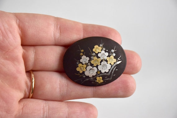 Zogan Plum Blossom Brooch shown close up in a hand for scale highlighting the detailed floral pattern