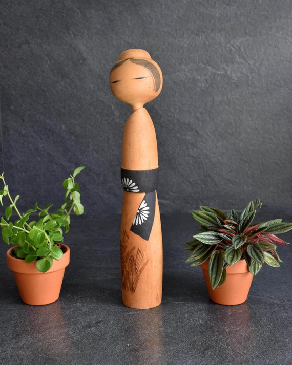 Sato Suigai Minatsuki Kokeshi Doll standing upright between two small potted plants