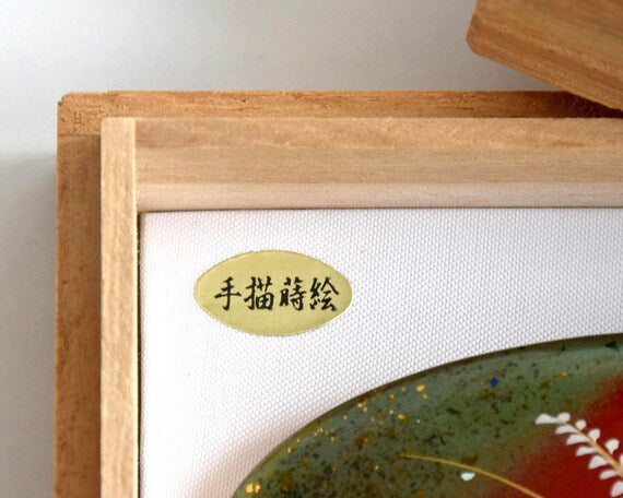 Maki-E Red Oval Barrette With Gold Floral showing a close-up of the small gold text label inside the box