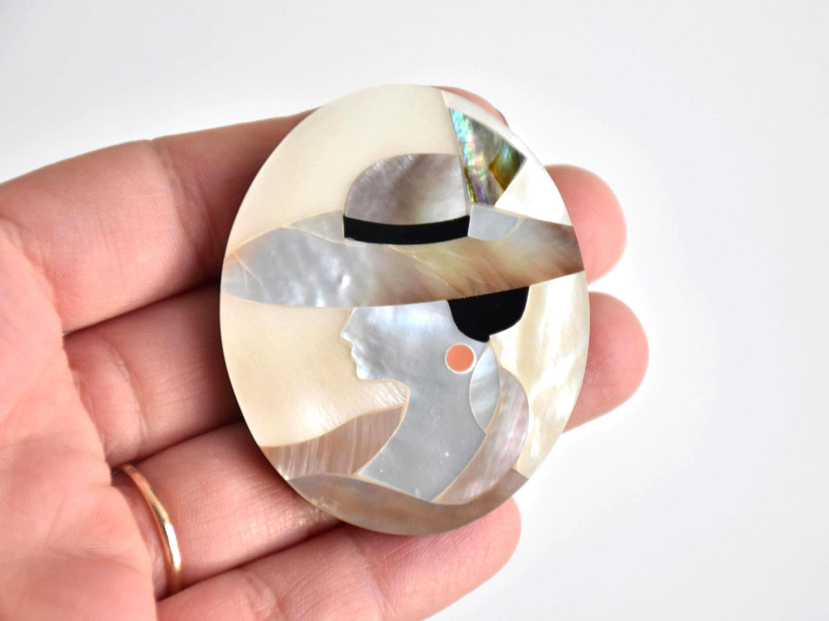 Raden Shell Inlay Portrait Brooch Woman With Hat shown next to a hand for size scale