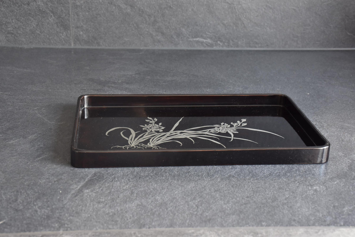 Black lacquer serving tray shown from a low angle resting on a dark slate countertop surface