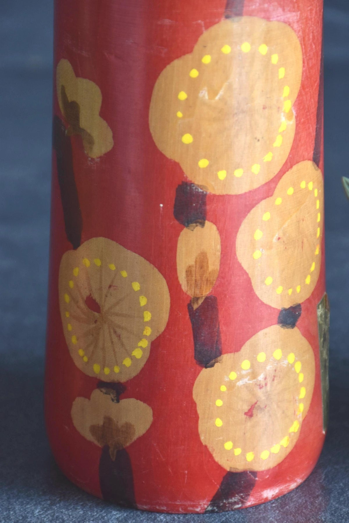 Hakuho Sosaku Kokeshi doll pattern detail showing close up of hand-painted yellow blooming plum blossoms on red lacquer.