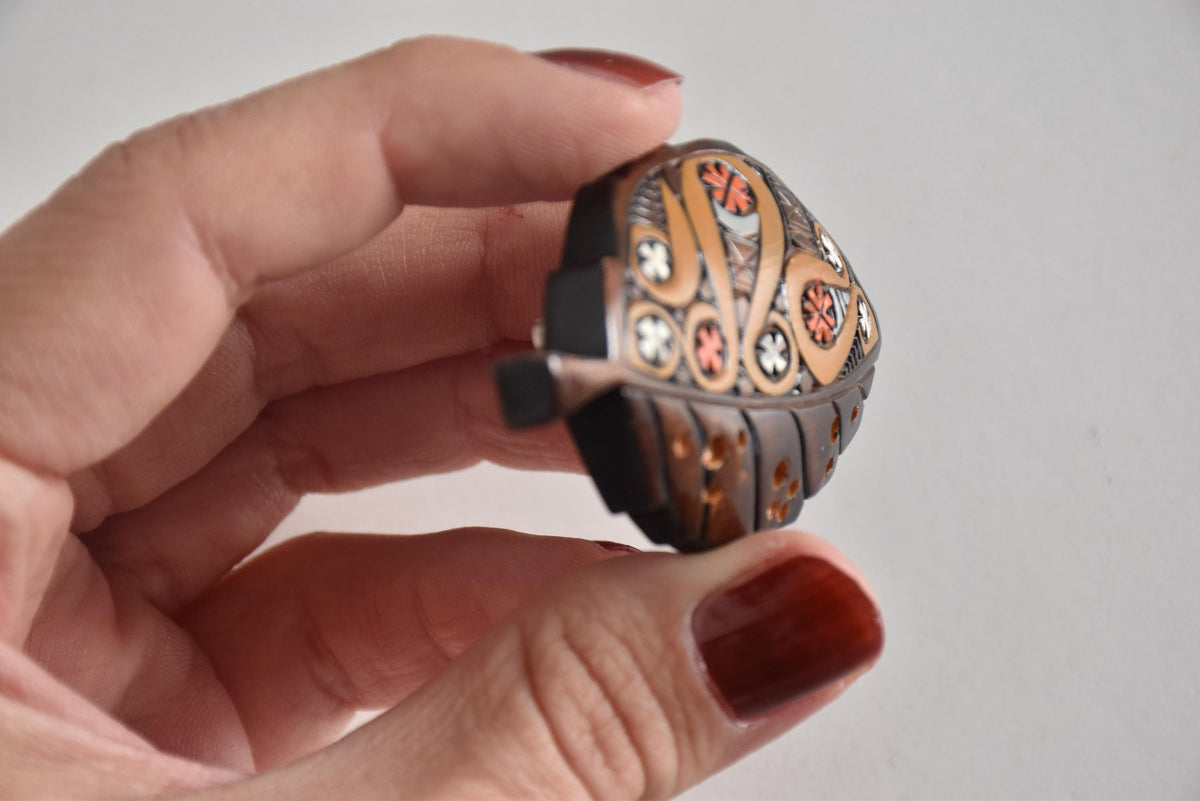 Angled view of Ainu leaf brooch held in hand highlighting carved stem