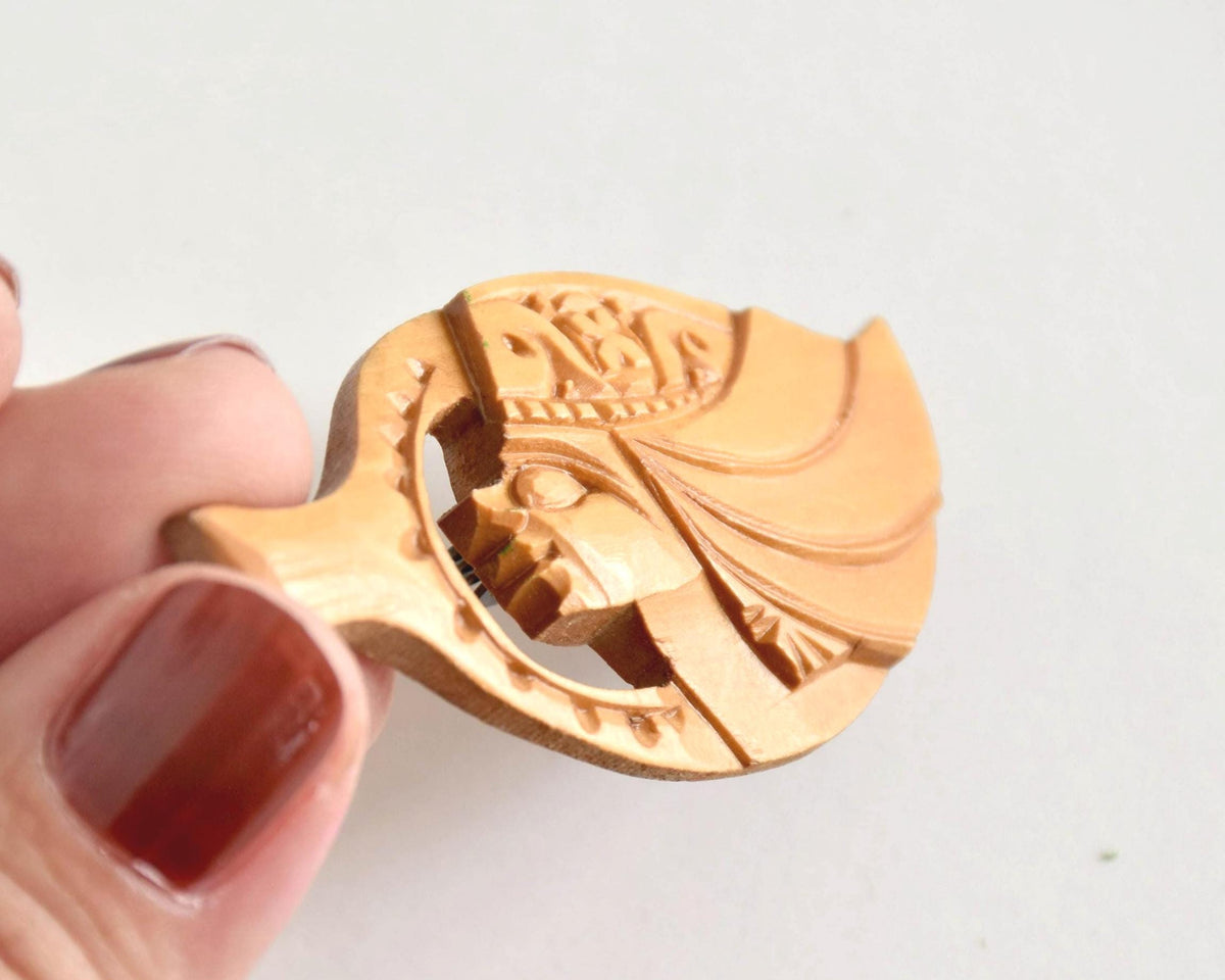 Ainu hand-carved wooden brooch held up near hand for scale