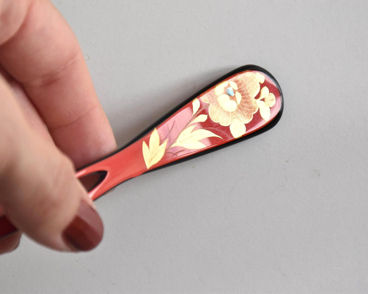 Red lacquered kanzashi hair accessory being held by hand to show detail