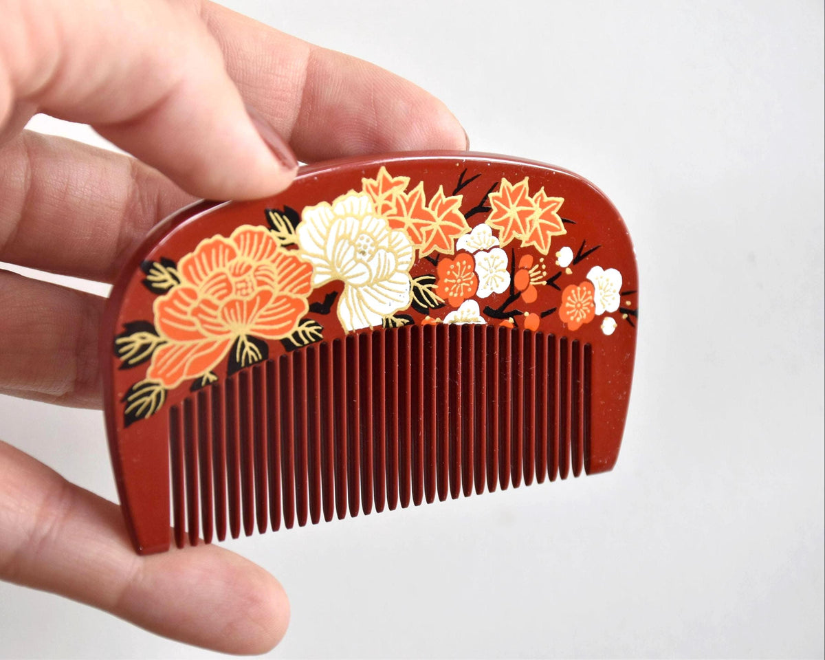 Toyama Urushi Kushi comb held next to a hand to show its actual size of 8.9 cm by 5 cm