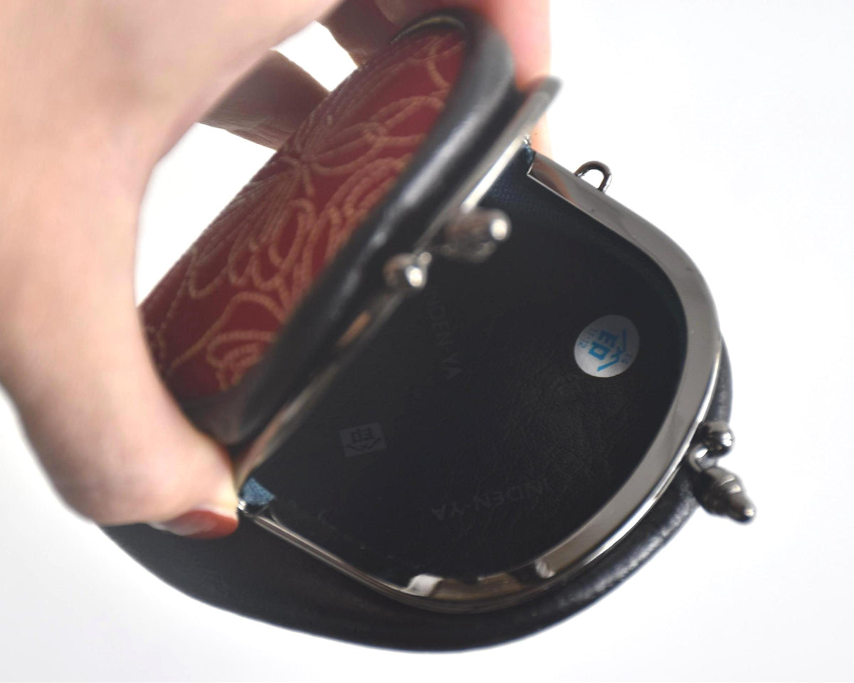 Inden deerskin coin purse held open by a hand revealing the dark interior lining and branding