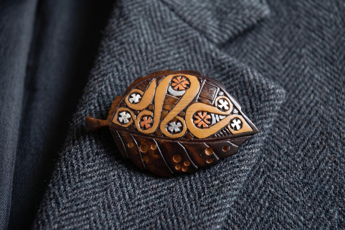 Ainu leaf brooch pinned to a dark gray herringbone jacket lapel