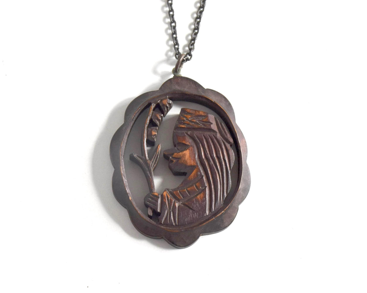 Ainu wooden pendant necklace hanging from a dark chain against a white background