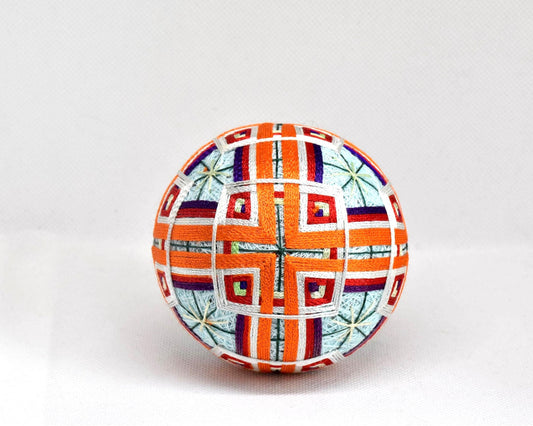 Japanese Temari ball showing a symmetrical geometric pattern in orange and white threads