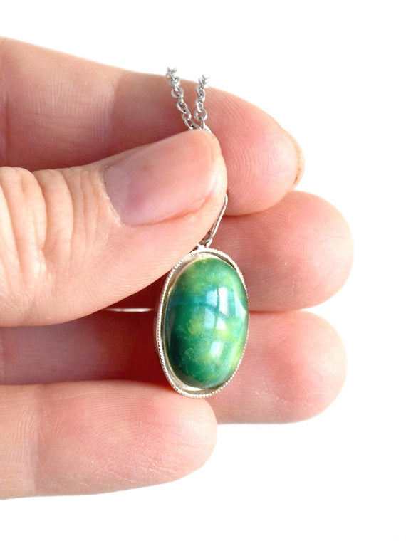 Green Oval Kutani pendant necklace held closely between fingers for detail