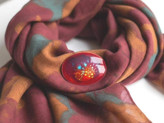 Kutani Dark Red Ceramic Brooch displayed on a patterned fabric scarf highlighting the dynamic red and turquoise fire pattern