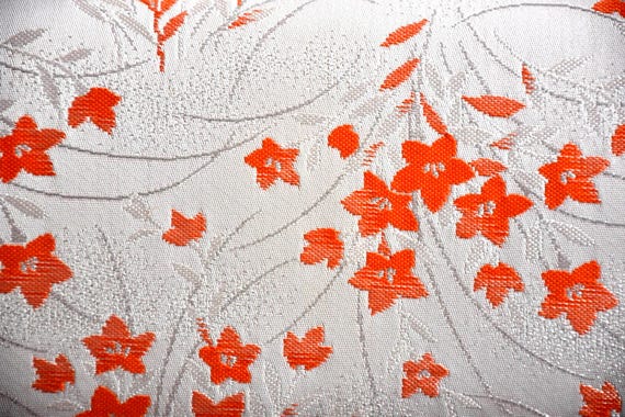 Kimono clutch fabric detail showing woven shimmering orange floral motifs on a soft pearly beige base