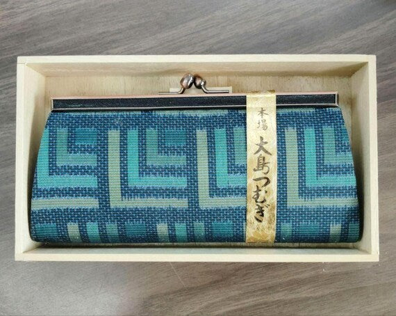 Oshima Tsumugi silk coin purse resting neatly inside the open wooden collector box