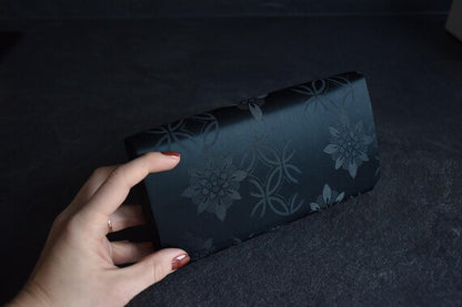 Black Floral Woven Clutch held in a hand showing the back exterior