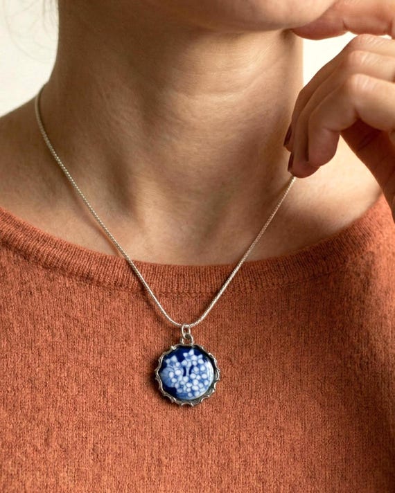 Kiyomizu-yaki Blue Floral Pendant Necklace worn on a person with a rust-colored top