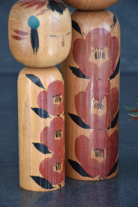 Takahashi Hashime kokeshi pair close up on the hand-painted red camellia blossom body designs