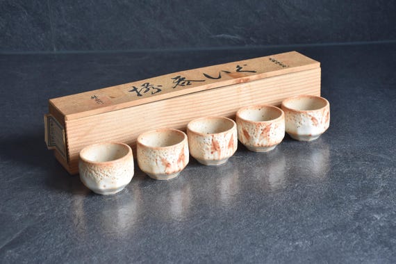 Set of 5 Shino ware guinomi sake cups arranged neatly in front of their wooden storage box