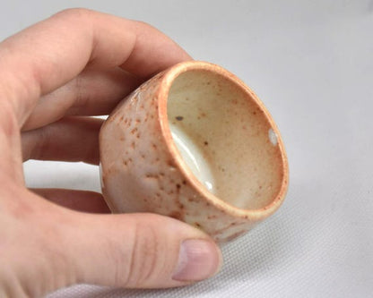 Shino ware ceramic guinomi sake cup held in a hand showing flat sides and size
