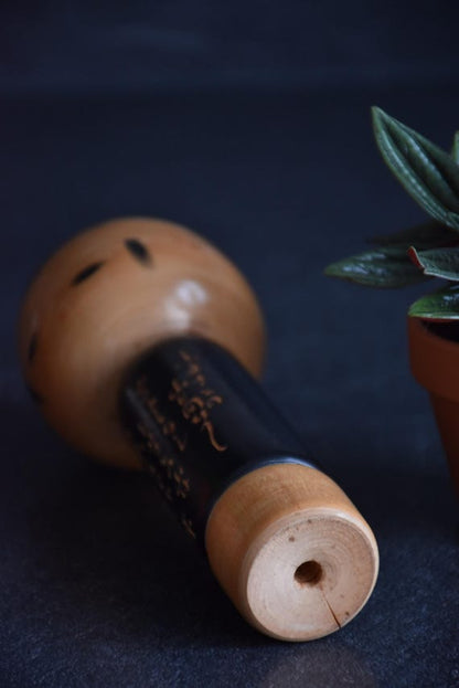 Vintage Japanese kokeshi doll with poem showing the wooden base with central hole detail.