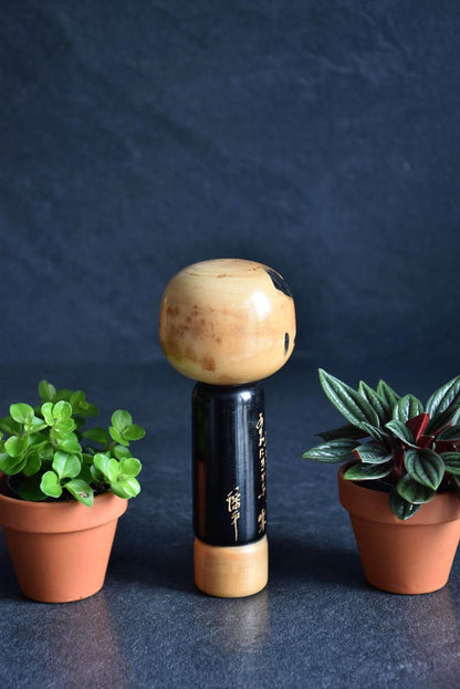 Vintage Japanese kokeshi doll with poem showing close-up of calligraphy details on the black body.