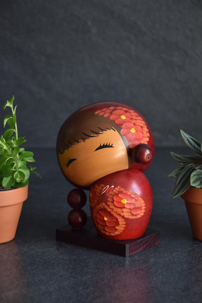 Chie Tamura Pigtail Kokeshi doll front view angled slightly to the right with potted plants