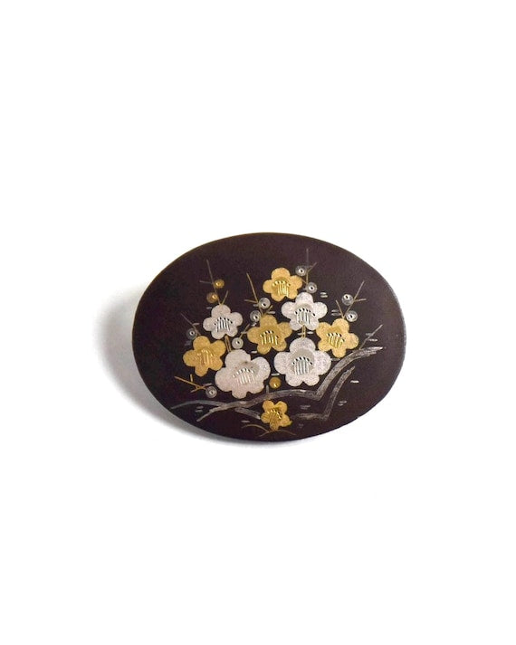 Zogan Plum Blossom Brooch laid flat against a neutral surface showcasing the precious metal inlay