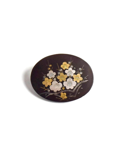 Zogan Plum Blossom Brooch laid flat against a neutral surface showcasing the precious metal inlay