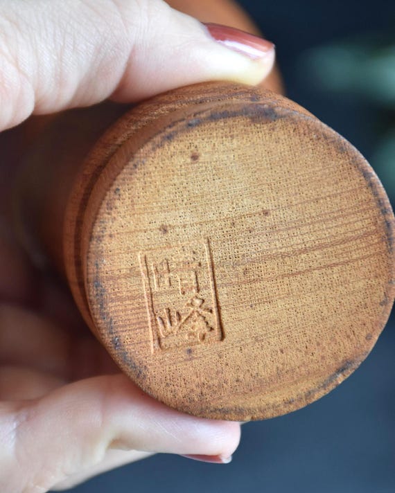 Aida Seihou kokeshi doll base held in a hand showing the stamped signature detail clearly