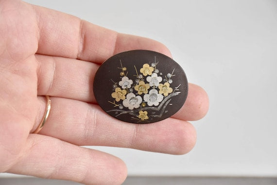 Zogan Plum Blossom Brooch displayed flat against fingers to show the oval shape and matte texture