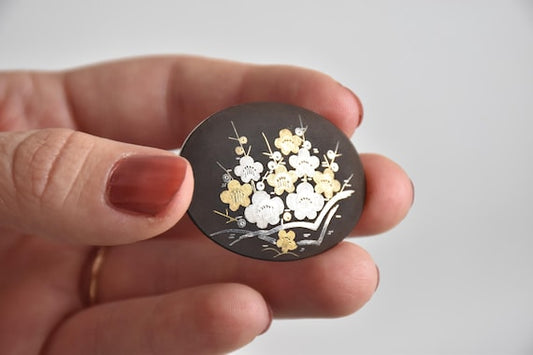 Zogan Plum Blossom Brooch featuring traditional Japanese Zogan metal inlay in silver and gold on a black background