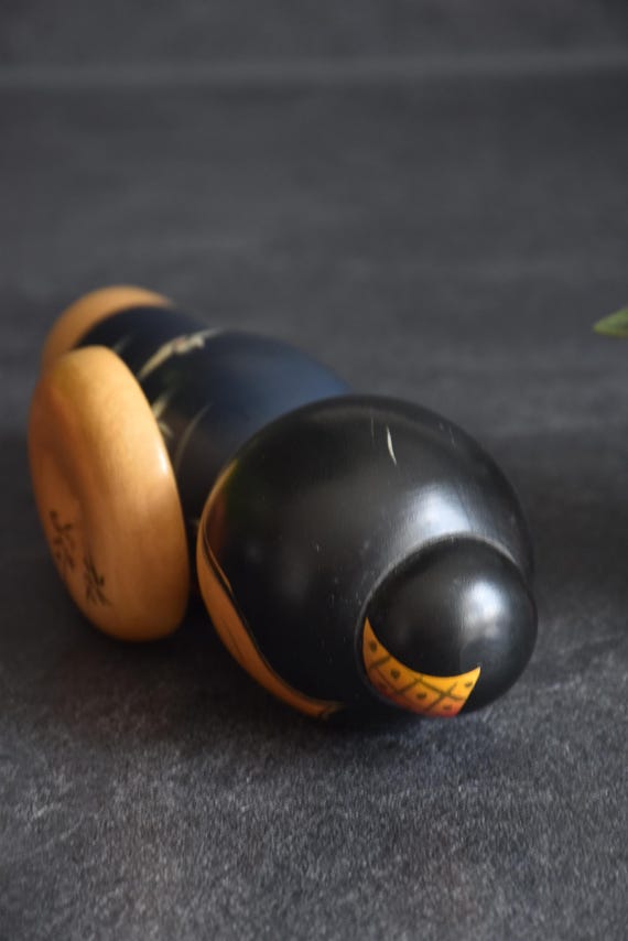 Miyashita Hajime kokeshi doll lying horizontally, showcasing the top of the head and hair ornament