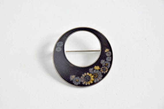 Zogan Floral Inlay Brooch front view showcasing the round dark metal base and gold floral design