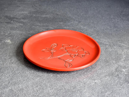 Murakami Kibori Tsuishu Camellia Red Lacquer Plate presented on a dark textured surface