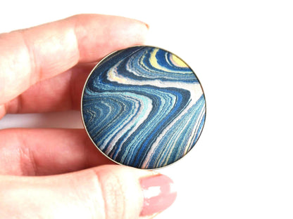 Suminagashizome marbled fabric brooch and pendant shown next to hand for scale