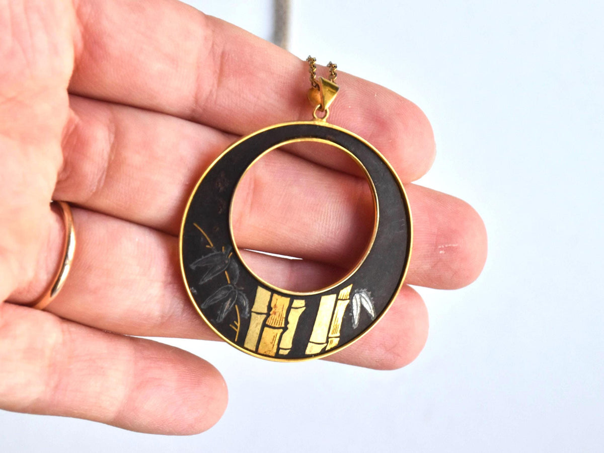Amita Damascene Pendant Necklace Bamboo Grove shown next to a hand for scale