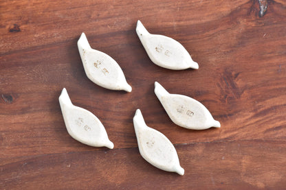 Ceramic leaf chopstick rests backs showing speckled texture on wood.