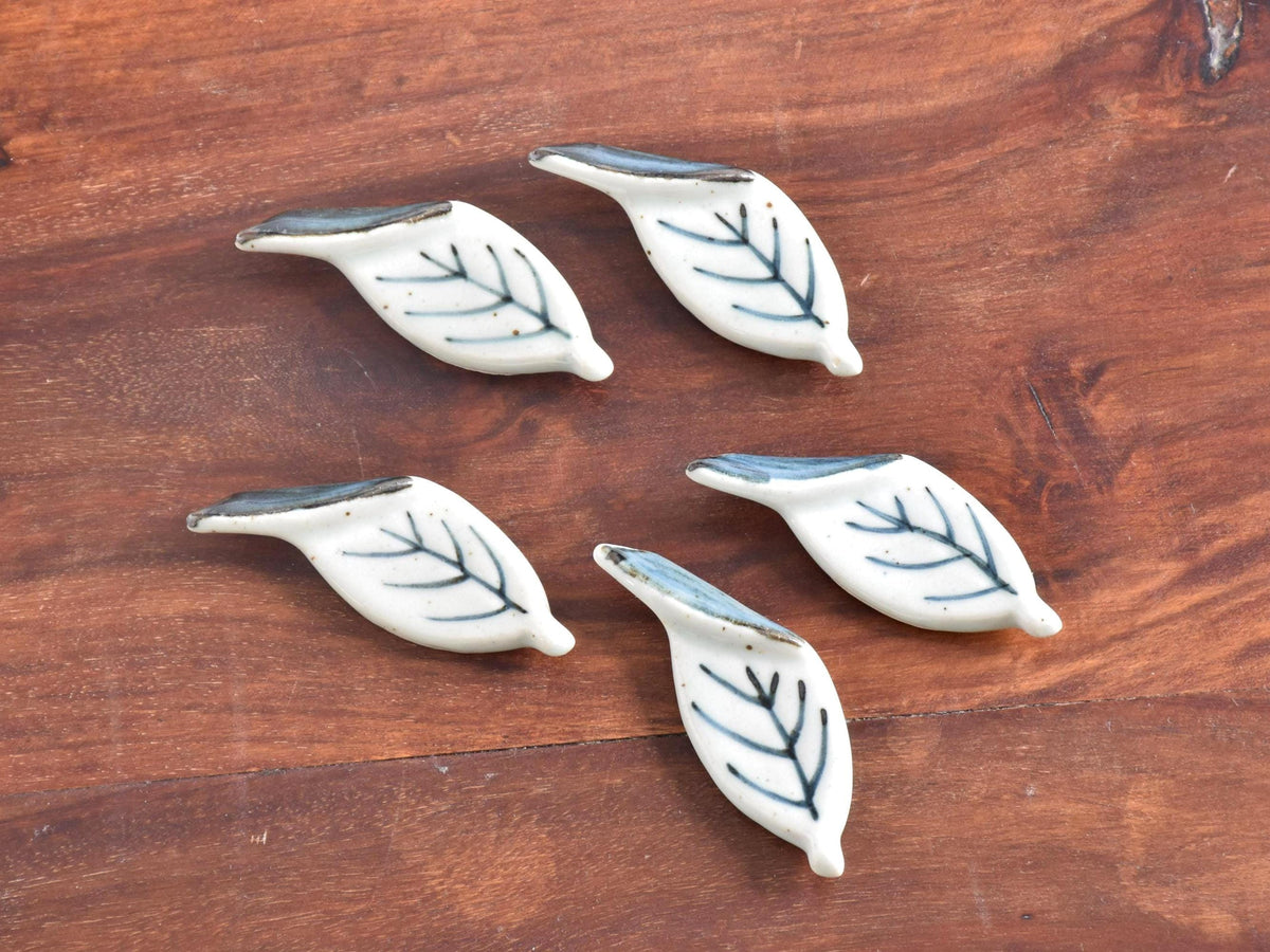 Ceramic leaf chopstick rests set arranged on a warm wooden background.