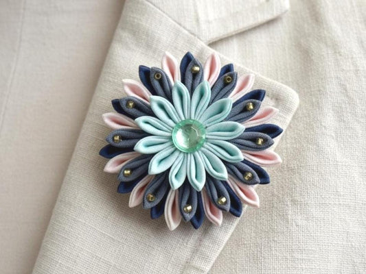 Tsumami Zaiku Turquoise And Cream Fabric Flower Brooch pinned to a cream jacket lapel