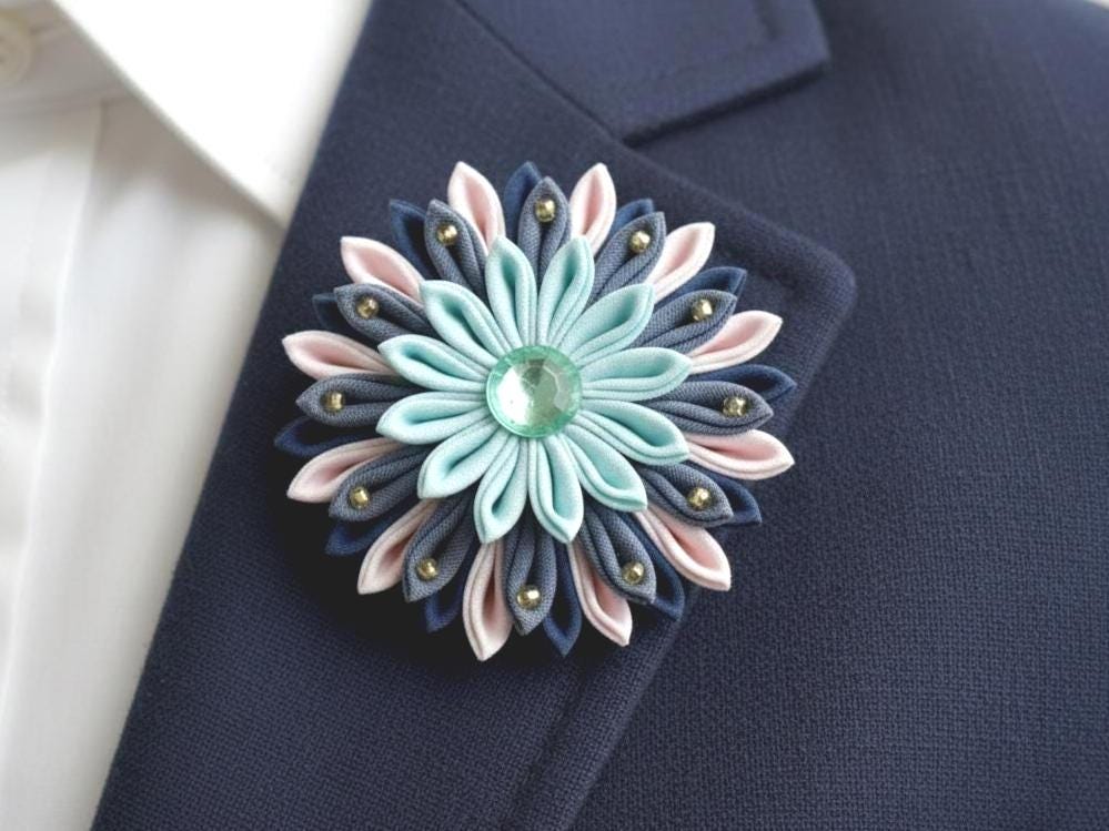 Tsumami Zaiku Turquoise And Cream Fabric Flower Brooch pinned to a dark blue jacket lapel