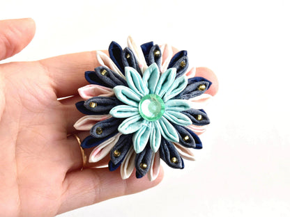 Tsumami Zaiku Turquoise And Cream Fabric Flower Brooch held next to a hand for scale