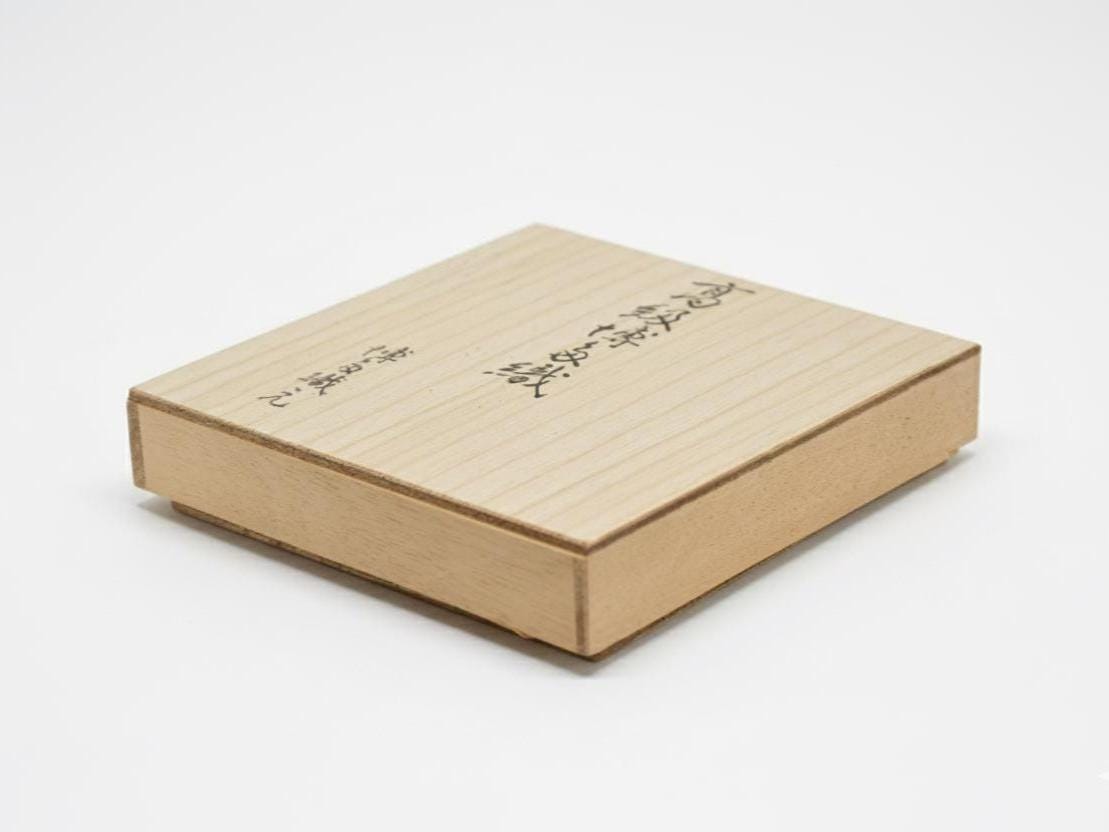 Vermilion Hakata-Ori Silk Clasp Coin Purse wooden storage box angled on a white surface