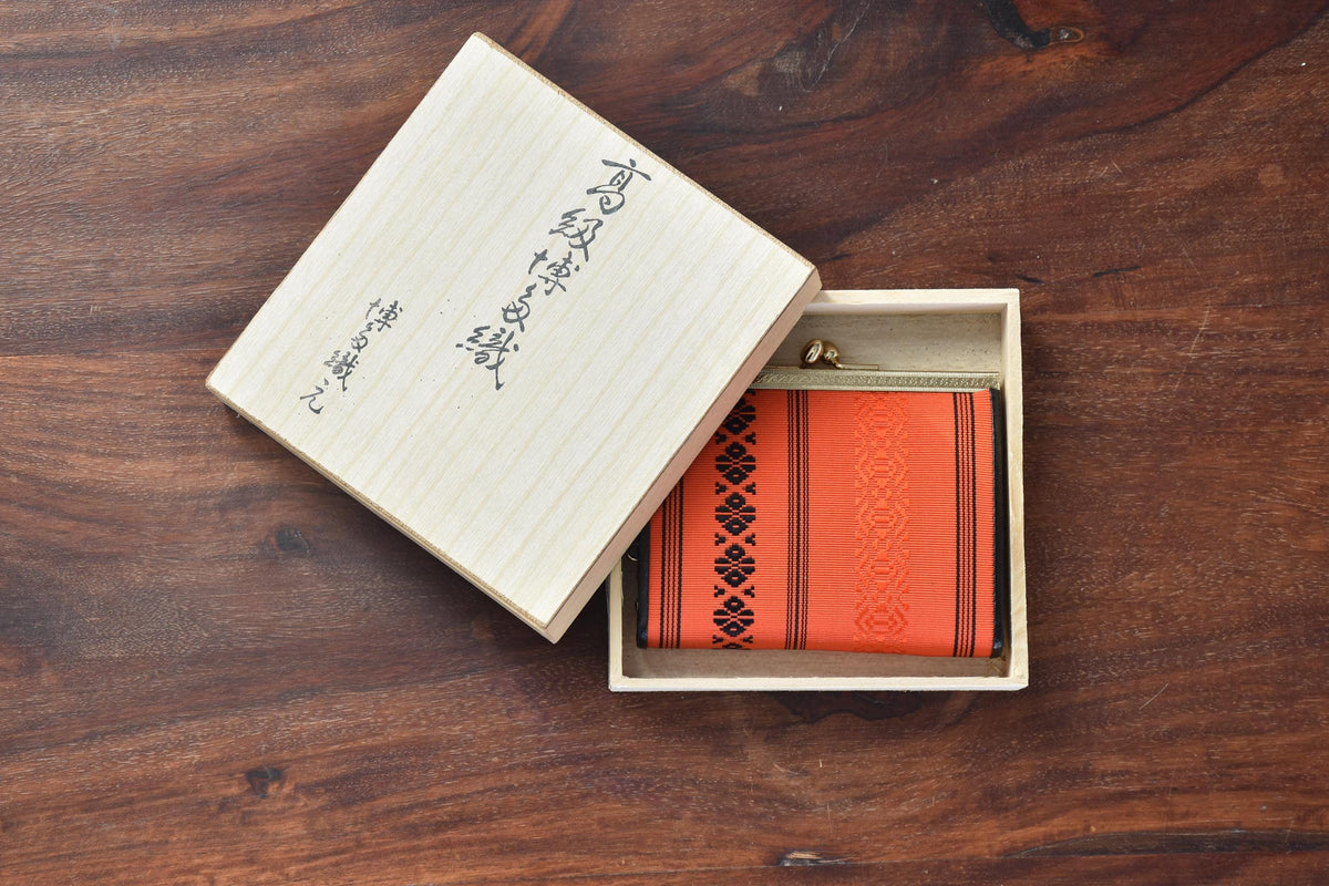 Vermilion Hakata-Ori Silk Clasp Coin Purse displayed partially inside its inscribed wooden box on a dark wooden surface