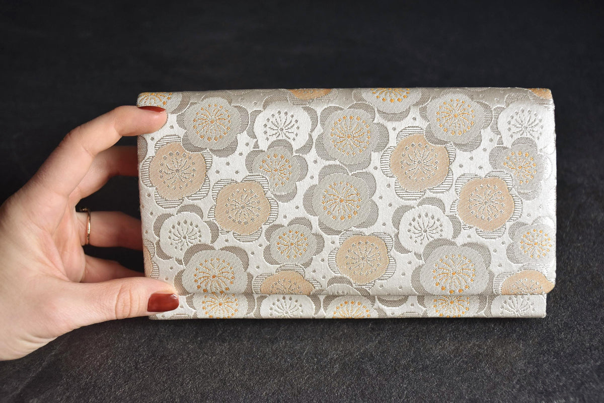 Nishijin-Ori silk clutch held in hand displaying scale and angle against dark surface