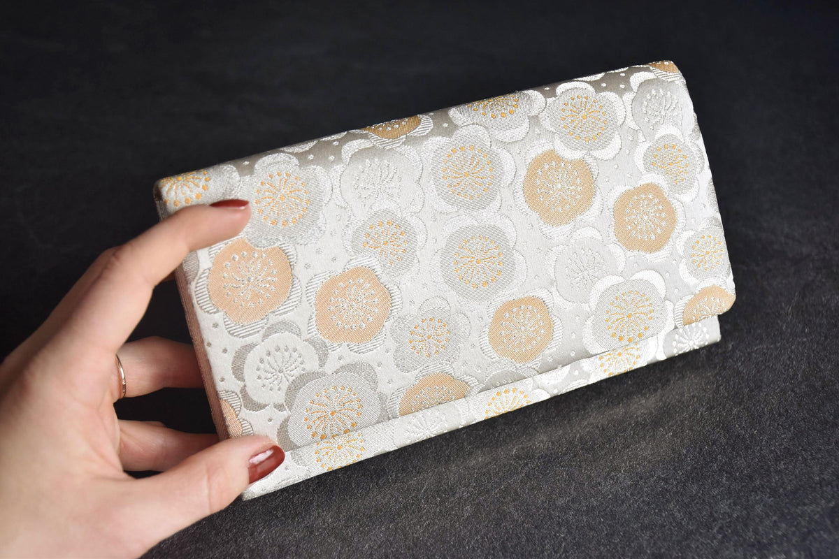 Nishijin-Ori silk clutch held in hand to show the size next to the fingers on dark background