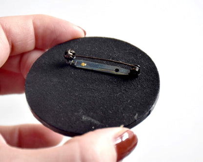 Japanese lacquerware floral brooch held up close to show the metal pin mechanism