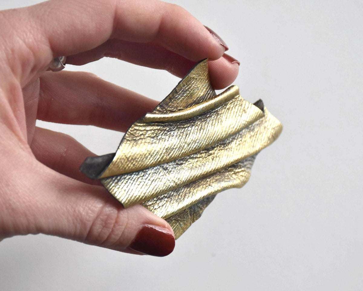 Sculptural leather brooch viewed from the side in hand to highlight depth and folded surface